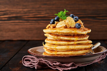 Pancakes with banana, walnut, honey and caramel for a breakfast on dark wooden background. Selective focus.