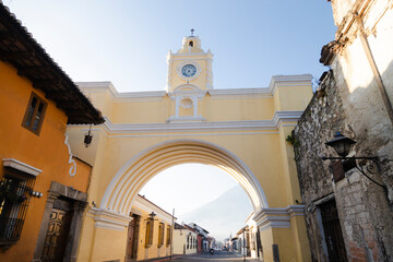 Arch of Santa Catalina and colonial houses in main avenue of Antigua Guatemala with water volcano in the background - yellow arch of colonial city in Guatemala early in the morning