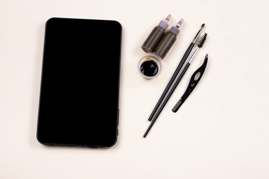 Mock up empty black tablet screen near a set for brow hena, tweezing procedure. Video tutorial, online fashion workshop. Skincare on beige background