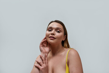 Obraz premium Portrait of sensual curvy young woman wearing yellow bra posing isolated over grey background