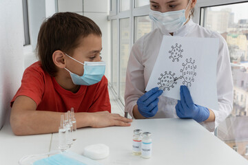 boy in medical mask looks on drawing of coronavirus in doctor's hands. Doctor immitates injection  and explains vaccination process.