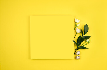 Easter composition. Easter eggs, flowers, paper blank on yellow background. Flat lay, top view, copy space, mock up.