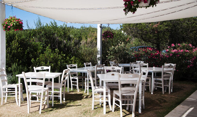 Rustic outdoor cafe with wooden white tables and chairs under the shelter