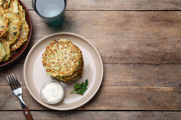 Delicious zucchini fritters with sour cream served on wooden table, flat lay. space for text