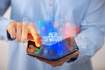 Young man holding a foldable smartphone with WEB SEMINAR inscription, educational concept