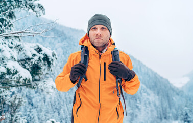 Man dressed bright orange softshell jacket with backpack have trekking on the winter mountains...