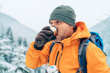 Fototapeta na wymiar Man drinking a hot drink from thermos flask dressed bright orange softshell jacket while he trekking winter mountains route. Active people in the nature concept image.