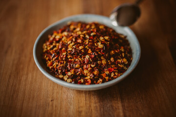 Red chili flakes in a bowl on wooden background. Red cayenne pepper.	