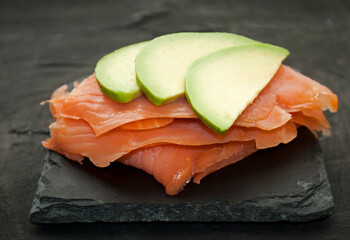 Fresh salmon, avocado  on a slate plate, black concrete background. Raw salmon tartare.