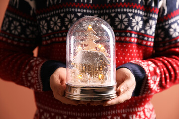 Man holding decorative snow globe on coral background, closeup