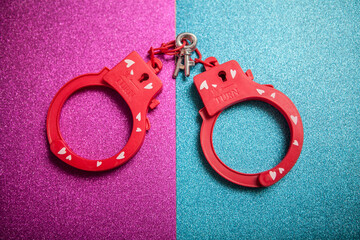 Red sex toy handcuffs on pink blue glitter background