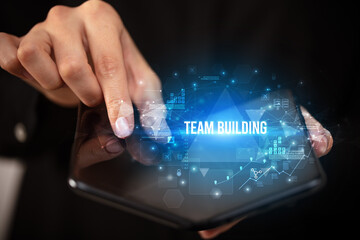 Businessman holding a foldable smartphone with TEAM BUILDING inscription, business concept
