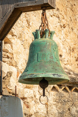 Obraz premium green copper bell on stone wall of Greek church Ekklisia Agios Ioannis hanging in the sunlight