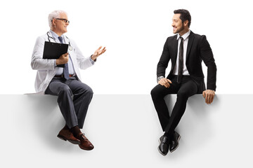Mature doctor seated on a blank panel gesturing and talking to a man in a suit