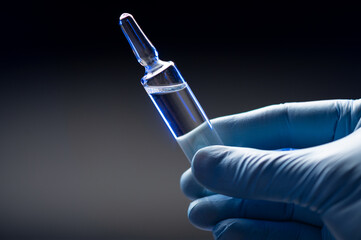 Hand in blue medical gloves holds an ampoule with a coronavirus vaccine. Coronavirus vaccination...