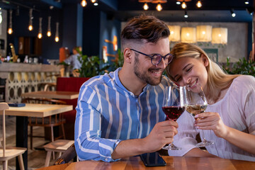 Happy young romantic couple in love, toasting with wine glasses at dinner in a beautiful restaurant.