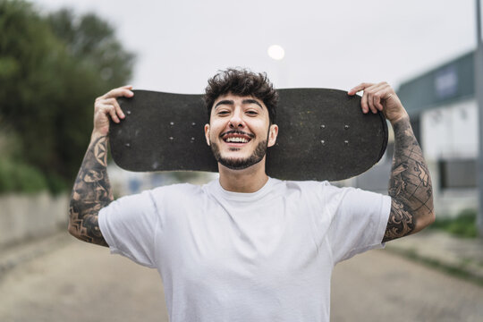 Shallow focus shot of a handsome smiling European skater posing with a skateboard in hands