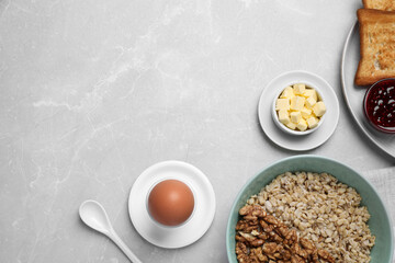 Tasty breakfast with oatmeal porridge, egg and toasts on light grey marble table, flat lay. Space for text