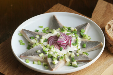 Herrings fillets with cream sauce with cucumbers, red onion and spices on cutting wooden board
