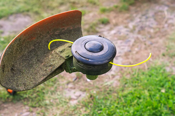 Close-up of the trimmer. A lawn mower reel with a yellow fishing line is lying on the grass. The coil of a manual lawn mower. A tool for cleaning the territory. Mow the grass on the plot.