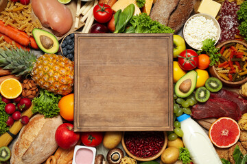 Wooden board on pile of different food products, top view with space for text. Healthy balanced diet