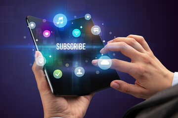 Businessman holding a foldable smartphone with SUBSCRIBE inscription, social media concept