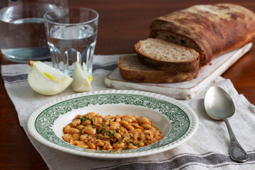 Bean stew, ciabatta and onions on a wooden table.