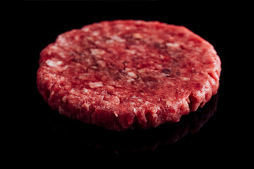 Closeup shot of a fresh raw burger patty on a black surface