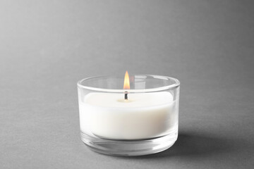 Fototapeta na wymiar Burning small wax candle in glass holder on grey background