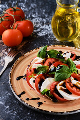 Tomatoes and mozzarella - vegetarian dish, Italian Caprese salad with tomatoes, mozzarella cheese, basil, balsamic vinegar and olive oil. On ceramic plate. Close-up, selective focus, marble dark table