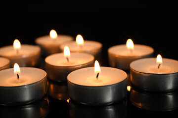 Fototapeta na wymiar Many burning candles on black table in darkness