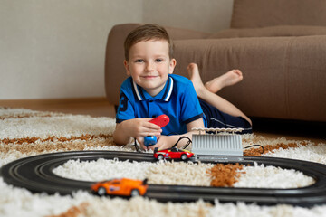 Boy plays with the race track on the remote control on the carpet