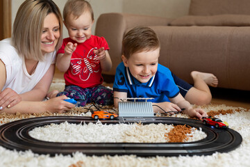 Mom and daughter and son play racing on the carpet.