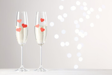 Glasses of champagne with paper hearts on white table against blurred lights. Space for text