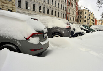 Snow covered cars parked at a street with classical architecture historical facades