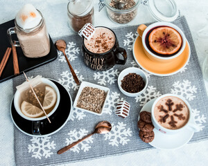 Obraz na płótnie Canvas Composition with various hot drinks, coffee, tea, cappuccino, cocoa on a tablecloth with snowflakes, cookies, cinnamon