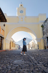 Fototapeta na wymiar Young Hispanic woman standing under the Arch of Santa Catalina in Antigua Guatemala - tourist on important avenue of colonial Guatemala city with the Water volcano background