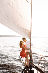 Couple in love holding on to a white sail and kissing on a yacht in the blue sea