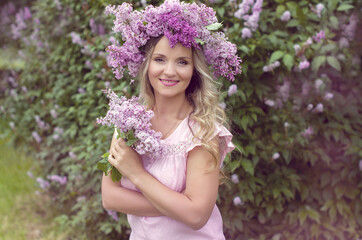 Blonde woman enjoying in a spring garden with blooming lilacs with bouquet, lilac flowers hair style.  Spring Concept, Spring blossom, Positive human emotions and feelings. 