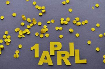 Inscription 1 April of yellow paper letters on a gray background, above the letters yellow confetti. High quality photo