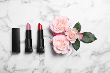 Obraz na płótnie Canvas Different lipsticks and beautiful flowers on white marble table, flat lay