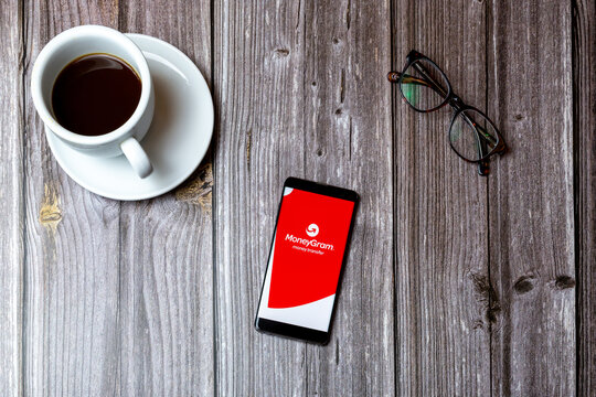 02/10/2021 Portsmouth, Hampshire, UK A mobile phone or cell phone laid on a wooden table with the moneygram app open on screen next to a coffee
