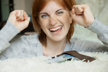 Happy young red-haired female with freckles received salary celebrate success with wallet full of money at home