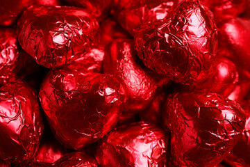 Tasty chocolate heart shaped candies in red foil wrappers as background, closeup