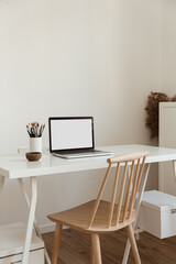 Laptop with blank copy space screen on table with stationery on table against white wall. Minimalist home office workspace. Mockup template.