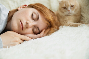 Close up pretty young red-haired female with ginger pet cat lying on bed sleeping relax in comfy bed