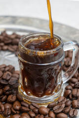 coffee being poured on a little glass, on a silver tray full of coffee beans