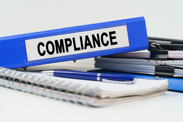 On the table are a notebook, a pen, documents and a folder with the inscription - COMPLIANCE