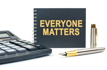 On a white background, there is a calculator, a pen and a black notebook with the inscription - EVERYONE MATTERS