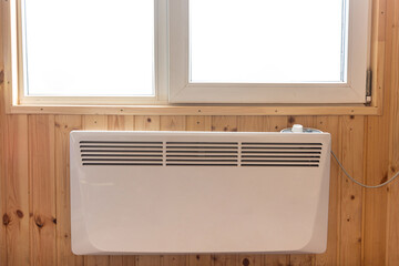 Electric radiator under the window of a country house whose walls are finished with clapboard